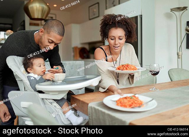 Couple eating spaghetti and feeding baby daughter at dining table