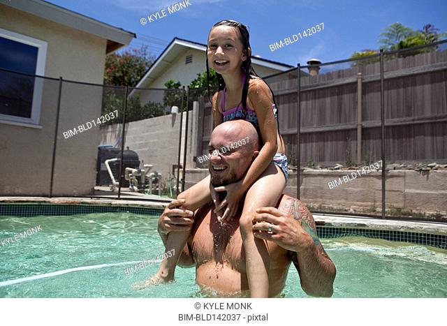 Caucasian father carrying daughter on shoulders in swimming pool