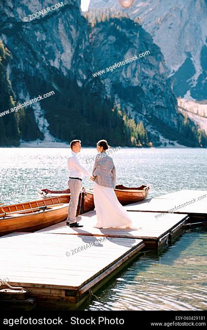 The bride and groom walk on a wooden boat dock at Lago di Braies in Italy. Wedding in Europe, at Braies lake. Newlyweds walk, kiss
