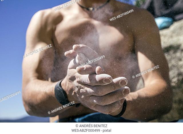 Shirtless climber coating his hands in powder chalk magnesium