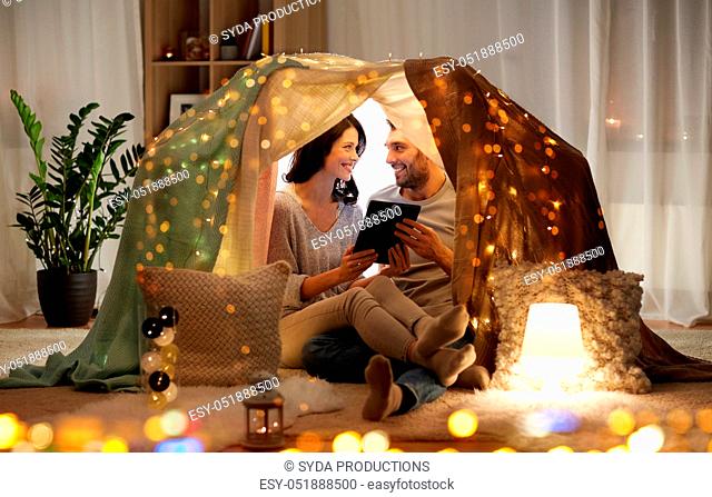 happy couple with tablet pc in kids tent at home