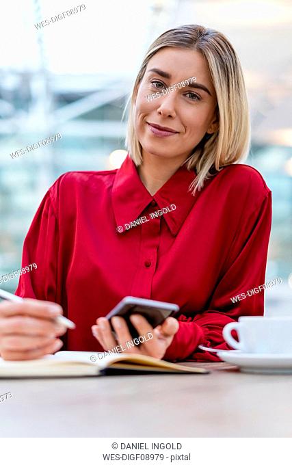 Portrait of young businesswoman with cell phone taking notes in a cafe