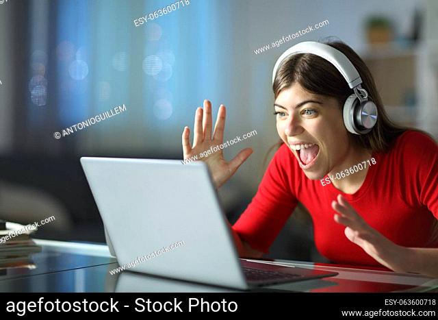 Excited woman watching media on laptop and headphone in the night at home