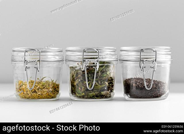 close up of jars with dried herbs on white table