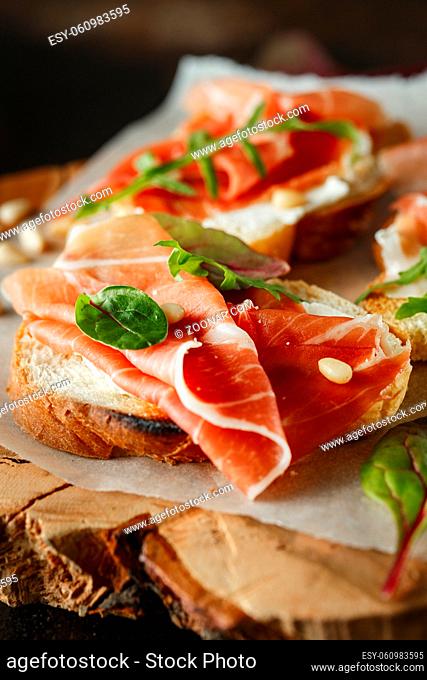 Traditional parma cured ham antipasto. Bruschetta set with Parma Ham and Parmesan Cheese. Small sandwiches with prosciutto, parmesan cheese, fresh arugula