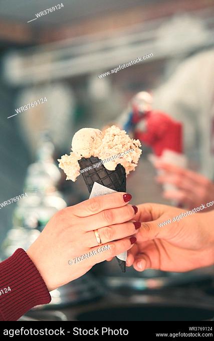 Woman buying couple scoops of ice cream in a candy shop by a street. Woman putting a scoops of ice cream to a cones