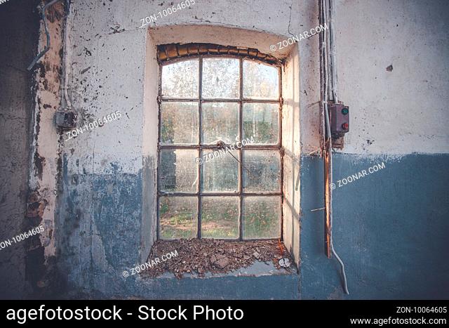 Dirty old window on a grunge wall with cracks and pealing blue paint with an electrical switch beside