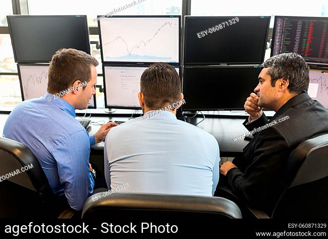 Businessmen brainstorming while looking at data on multiple computer screens in corporate office. Business people trading online