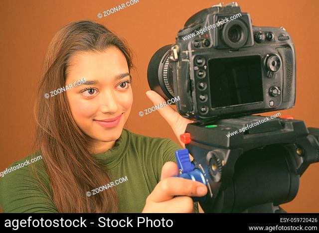 Studio shot of young beautiful Indian woman vlogging against brown background