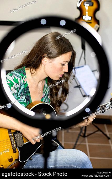 Young woman with webcam light playing guitar while sitting at home