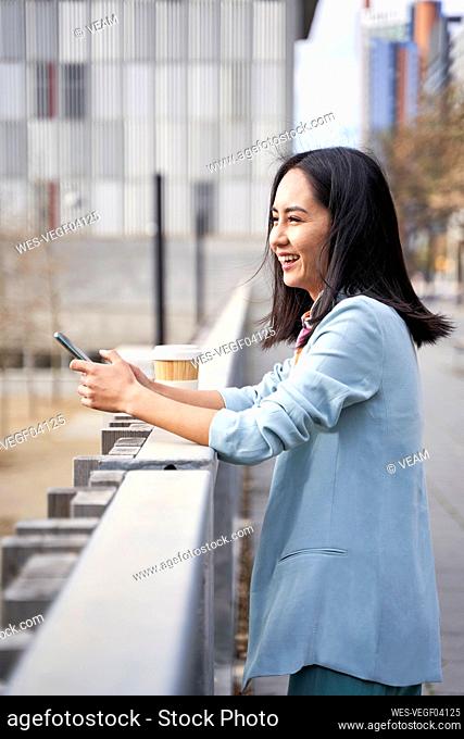 Businesswoman smiling and looking away while leaning on railing