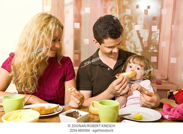 Junges Ehepaar sitzt am Frühstückstisch und füttert ihr Baby