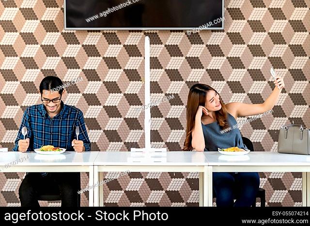 Asian couple take a selfie photo together in new normal social distance restaurant with table shiled partition to reduce infection of coronavirus covid-19...