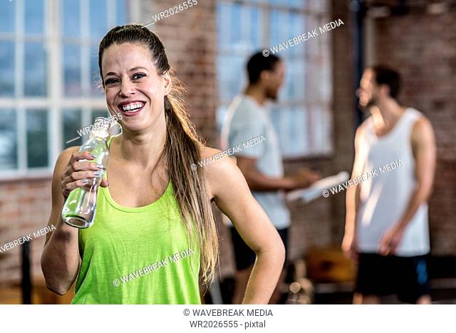 Young woman drinking water from a bottle with colleagues behind her