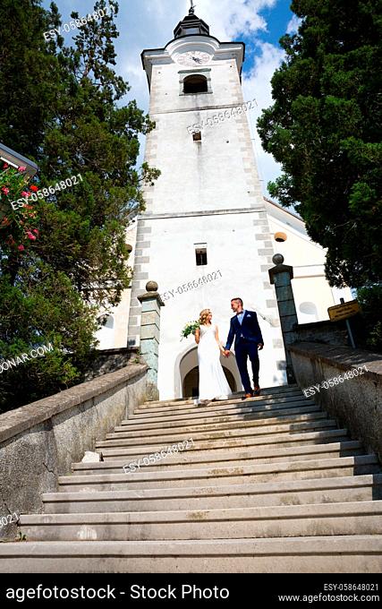 The Kiss. Bride and groom holding hands walking down the staircase in front of a small local church. Stylish wedding couple kissing