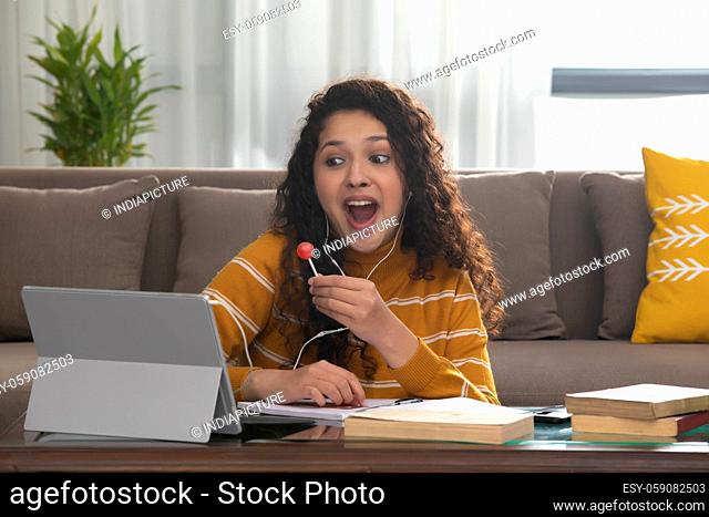 A HAPPY TEENAGER EATING LOLLIPOP DURING ONLINE CLASS