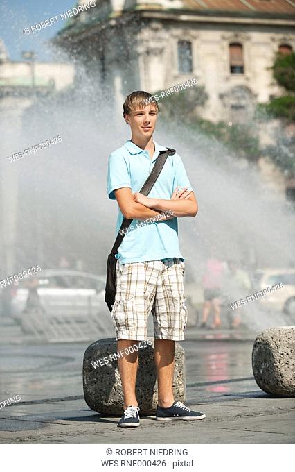 Germany, Munich, Karlsplatz, Young man standing at fountain