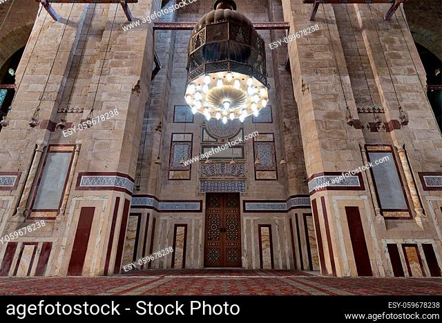 Cairo, Egypt - December 16, 2017: Old decorated bricks stone wall with colored marble decorations, big brass chandelier, and ornate wooden door in al Rifai...
