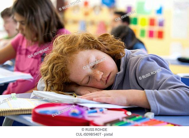 Primary schoolgirl asleep at desk in classroom