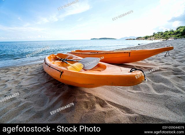 Two colorful orange kayaks on a sandy beach ready for paddlers in sunny day. Several orange recreational boats on the sand