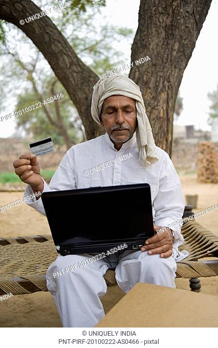 Farmer holding a credit card and using a laptop, Hasanpur, Haryana, India