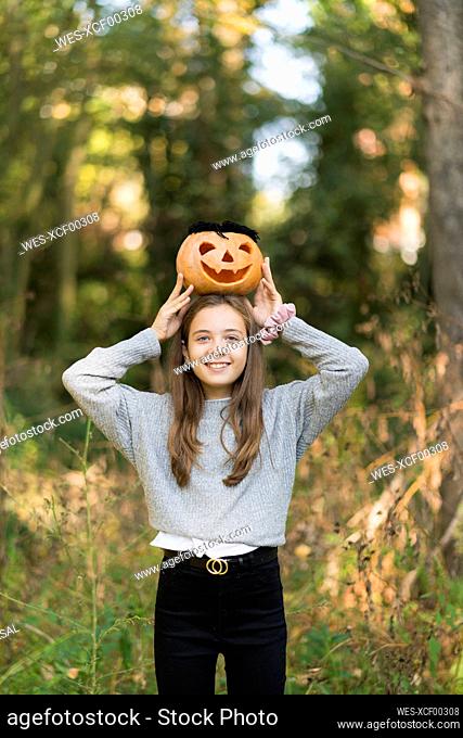 Playful girl holding Halloween pumpkin while standing at park