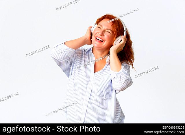 Emotions, lifestyle and leisure concept. Carefree laughing middle-aged woman with red hair, enjoying listening music, smiling pleased and relaxed