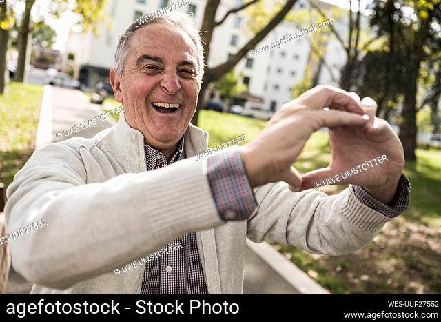 Happy senior man making heart shape with hand on footpath