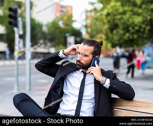 Portrait of bearded businessman sitting on bench and talking on smart phone