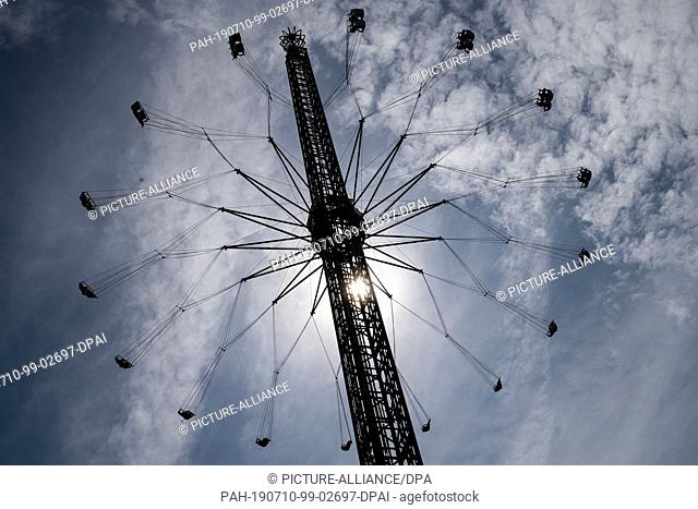 10 July 2019, North Rhine-Westphalia, Duesseldorf: A chain carousel on the Rheinkirmes can only be seen as a silhouette. The largest fair on the Rhine opens...