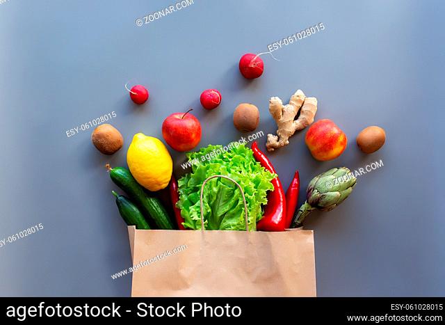 Healthy and organic food flay lay concept on gray background. Eco bag with scattered lettuce salad leaves, apples, kiwi, radish, lemon, cucumber, artichoke