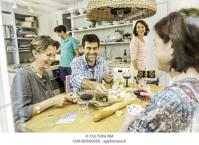 Five adult friends playing cards at dining table