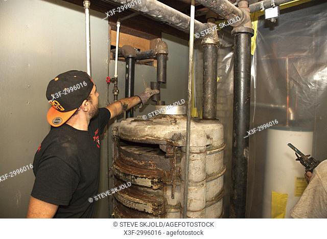Removing heating water pipes from old gravity style gas furnace during replacement process. St Paul Minnesota MN USA