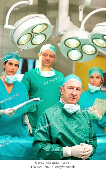 Surgeon sitting while crossing his hands with a team behind him in a surgical ro