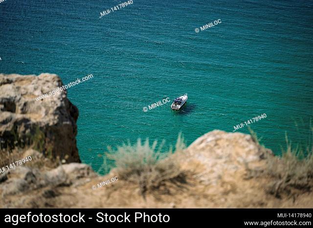 Lonely yacht boat moored in bounty lagoon, Cape Fiolent in Balaklava, Sevastopol, Russia. View from the top of the rock. Azure emerald gree sea water on sunny...