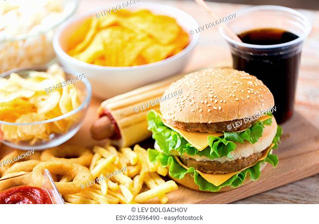 fast food and unhealthy eating concept - close up of hamburger or cheeseburger, deep-fried squid rings, french fries, drink and ketchup on wooden table