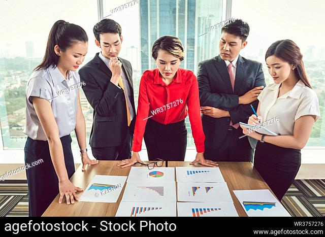 Group of businesspeople analyzing different business charts arranged on desk at workplace