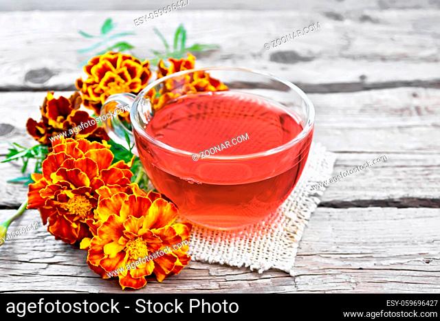Marigold herbal tea in a glass cup, fresh flowers on a napkin of burlap on background of an old wooden board