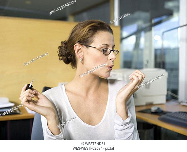 Woman in office, applying nail polish, blowing, close-up