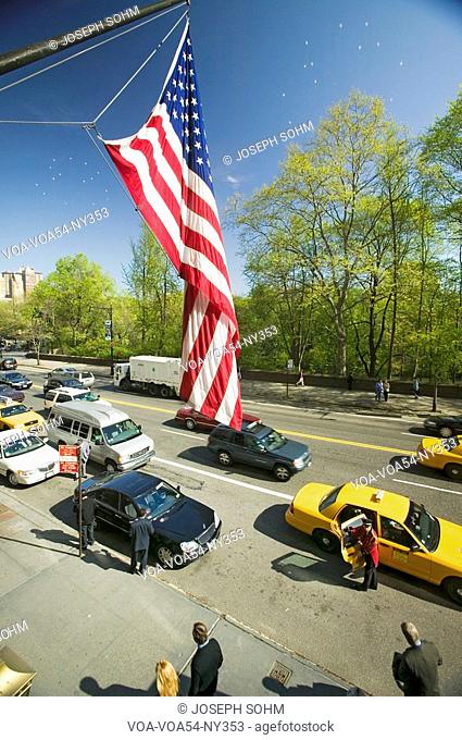 American Flag flies over Central Park in spring with yellow taxies in front of Helmsely Park Lane, Manhattan, New York City, NY