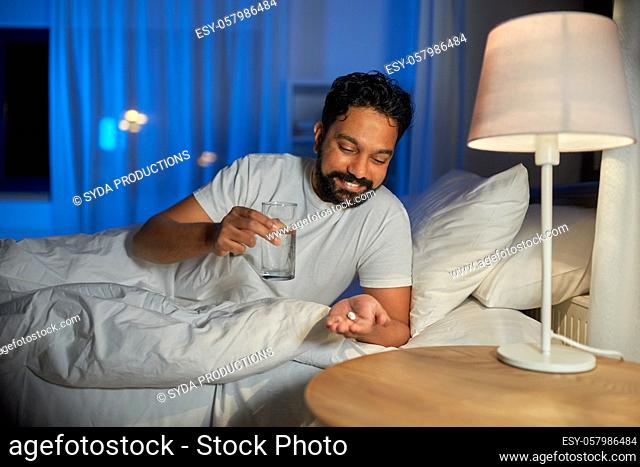 indian man with medicine and water in bed at night