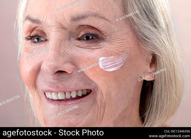 Studio shot of smiling senior woman with face cream