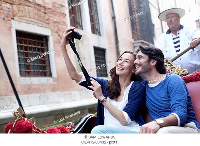 Smiling couple taking self-portrait with digital camera in gondola on canal in Venice