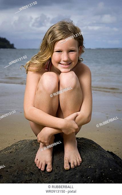 Portrait of a girl sitting on a rock and hugging her knees
