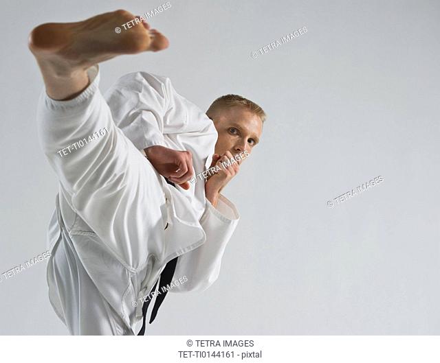 Young man performing karate kick on white background