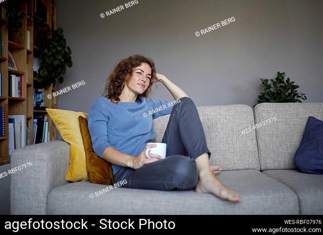 Thoughtful woman with head in hands sitting on sofa at home
