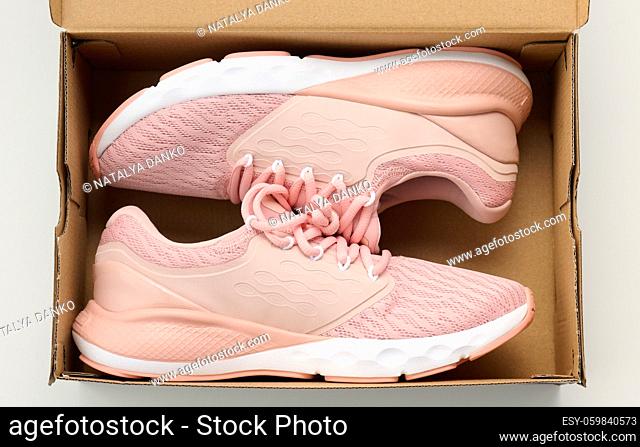 pair of pink textile sneakers in an open brown paper box on a white table, top view