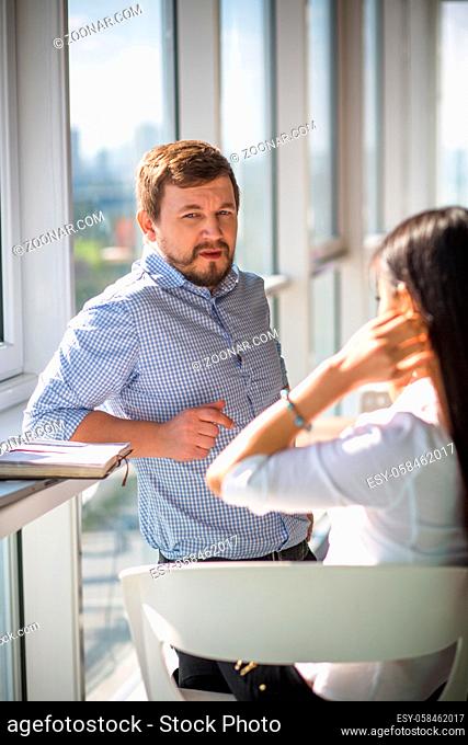 Businessman talking to his colleague businesswoman while working in office interior. Workers communicating about boss, every day things or relatives