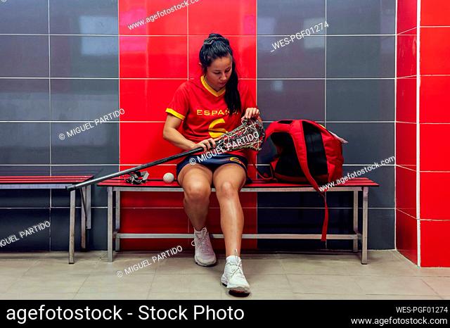 Young athlete adjusting string of lacrosse stick head in locker room