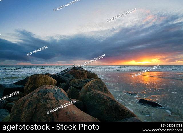 Sunset on the beach in Denmark. Stone groyne in the foreground. Walk on the coast in the sand. Landscape photo by the sea